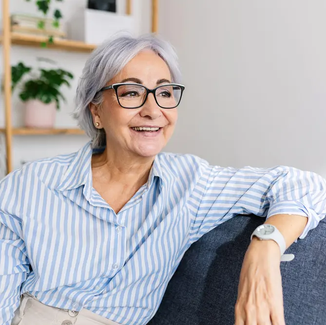 زن میانسال خندان و بانشاط که با حالتی آرام روی مبل خانه استراحت می‌کند. بانوی مسن شاداب که روی کاناپه نشسته و به دوردست نگاه می‌کند. فضای خالی برای متن.