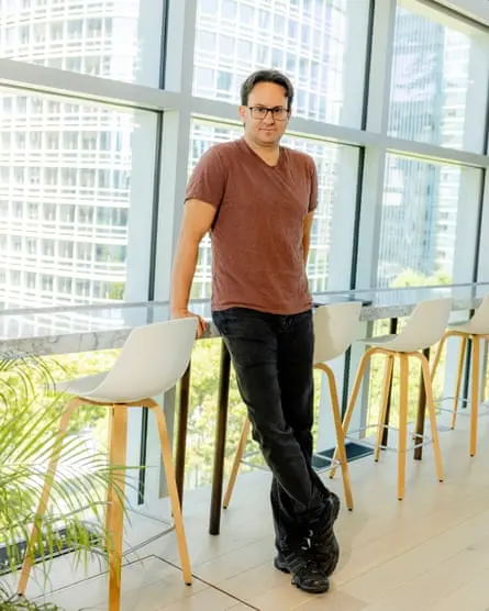 کاپلان پشت یک میزی که نزدیک به پنجره‌های بزرگ با نمایی از آسمان‌خراش است